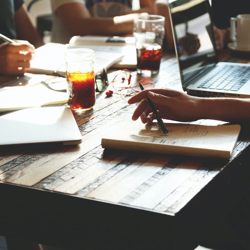Image of a community networking event of business owners sitting at a table with notebooks and laptops. Social media management for service based small businesses. Image by startup stock photos